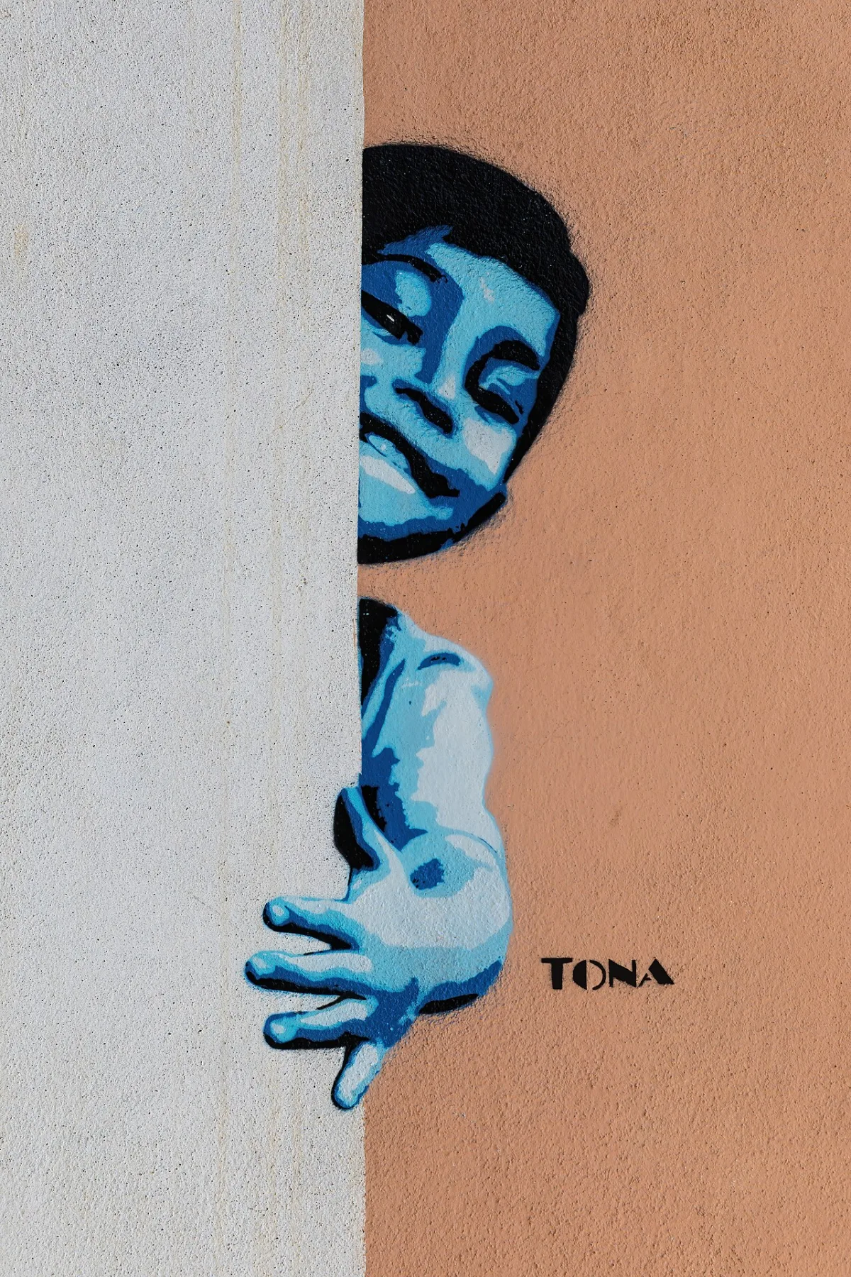 Blauwe stencil-muurschildering van een jongen die om een hoek gluurt op een gepleisterde muur